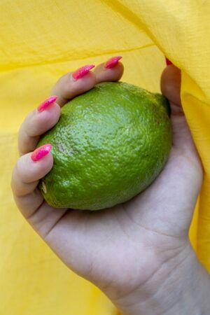 pink shiny manicure with silver glitter with lime in hand on a yellow backgroundの写真素材