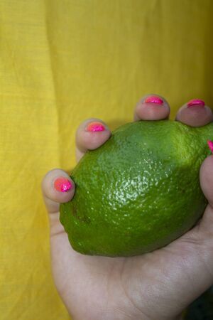 pink shiny manicure with silver glitter with lime in hand on a yellow backgroundの写真素材