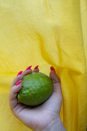 pink shiny manicure with silver glitter with lime in hand on a yellow backgroundの写真素材