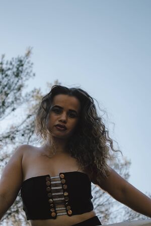 Woman with black top and curly hair with the sky in the background with trees.の写真素材