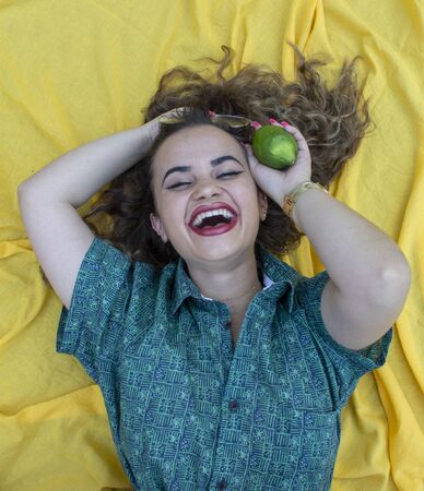 Young woman lying on yellow cloth as background. With curly brown hair.の写真素材