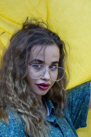 Portrait of beautiful young woman with glasses and disheveled hair. With urban fashion on yellow cloth background.の写真素材