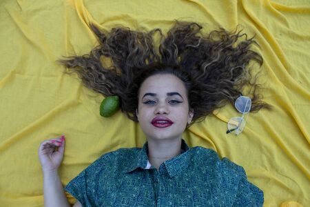 Young woman lying on yellow cloth as background. With curly brown hair.の写真素材
