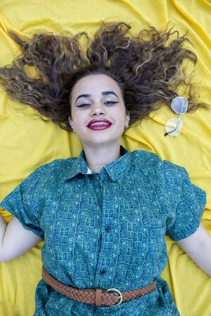 Young woman lying on yellow cloth as background. With curly brown hair.の写真素材