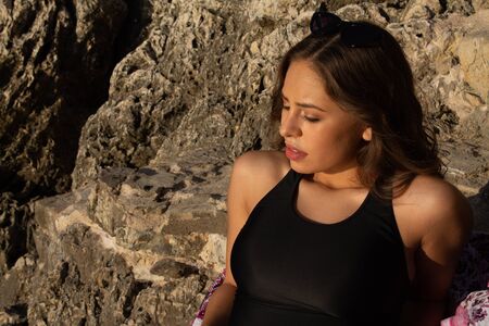 Young hipster woman lying on the rocks in a swimsuit over beach towel. Young woman lying near the...