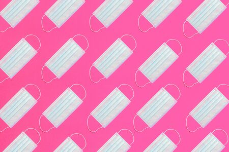 Many medical masks on the pink colored background to cover the mouth and nose for protection from virus and bacteria on a pink background. Epidemic concept. Regular pattern, flat lay.の写真素材