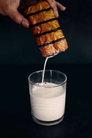 hand dipping pain au chocolat chocolate bread, Neapolitan or chocolate croissant in glass of milk , concept of processed foodの写真素材