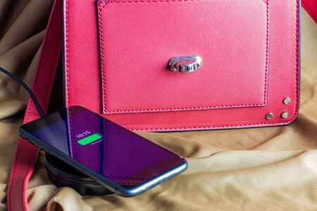 mobile with wireless charger next to modern red bag. Wireless charging concept and modernity.