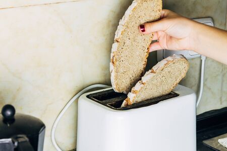 Woman toasting slices of bread for toast in the morning. Concept of breakfast and balanced meal and diet.の写真素材