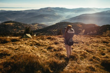 Young woman taking picture of a foggy valley from the top of Le Hohonck, Vosges mountains near Schiessrothried lake, France.の写真素材