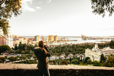 Sunset in Malaga, Spain. Woman photographer shooting the sunset on the docks and spanish city. Mediterrenean town and sea in the background.の写真素材