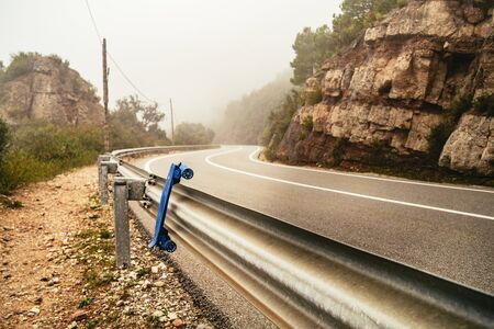 Blue skateboard on crash barriers at the side of a winding mountain pass in misty weather in the Monestir de Montserrat Region near Barcelona Spainの写真素材