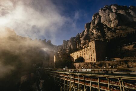 View of the Montserrat Monastery in the Monestir de Montserrat Region near Barcelona Spain with steep rocky cliffs towering above the building viewed over the bridgeの写真素材