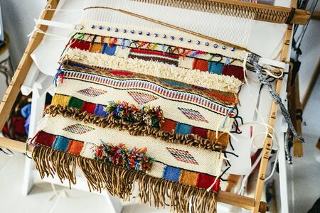 Colorful hand-woven tapestry on a small wooden hand loom with brightly colored stripes and geometric designsの写真素材