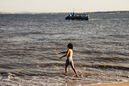 Young man tossing stones into the sea at sunsetの写真素材