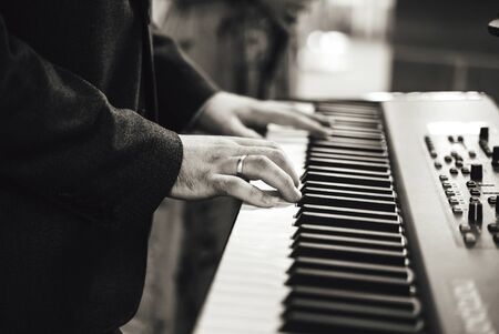 Black and white photo of mans hand playing on electronic keyboards. Shallow depth of field. Music,...