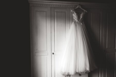 Black and white photo of wedding gown on hanger hanging on white wardrobe and waiting for bride. Wedding day concept.の写真素材