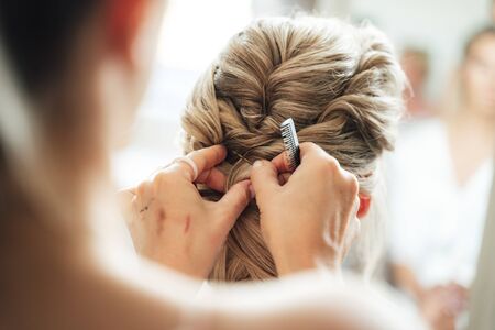 Hairstylist making bride wedding hairstyle. Rear view close up of hairdressers hands. Wedding day concept.の写真素材