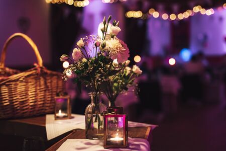 Evening shot of beautiful flowers in glass vase standing on a table. Floral decoration at wedding or...