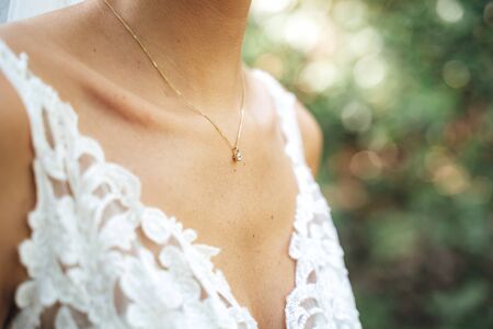 Close up of caucasian brides chest in white lace wedding dress. Neckline decorated with golden necklace with gemstone. Wedding day concept.の写真素材