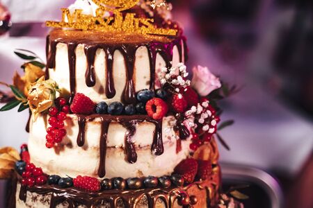 Close up of top of wedding cake decorated with dripped chocolate and various colorful berries. Sweet...