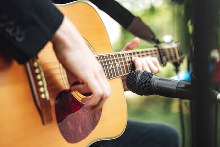 Man playing guitar. Closeup of male hands playing acoustic guitar. Outdoor background.の写真素材