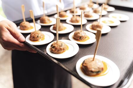Roasted meatballs served on small white plates. Male hands holding black tray. Selective focus....