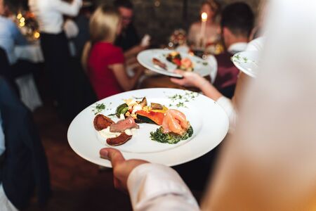 Man holding white plate with food got from self-service buffet table. Celebration, party, birthday or wedding concept.の写真素材