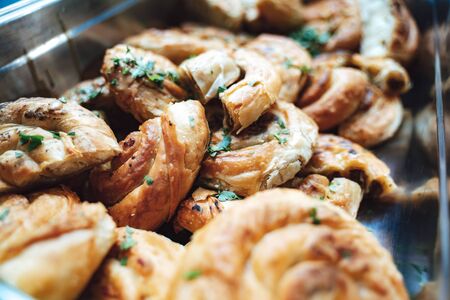 Pile of cheese and bacon swirls in stainless steel box. Baked salty snack. Self-service buffet...