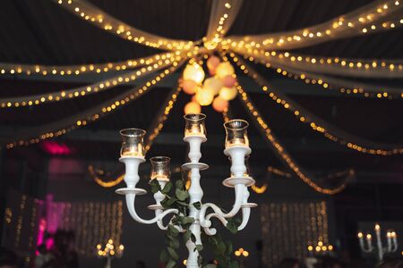 White vintage candelabrum with glass lamps and candles. Ceiling party lighting decoration. Evening...