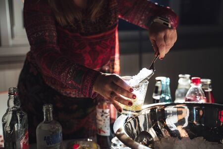 Woman preparing drink. Closeup of female hands putting ice info beverage at bar table. Celebration, birthday, party, wedding concept.の写真素材