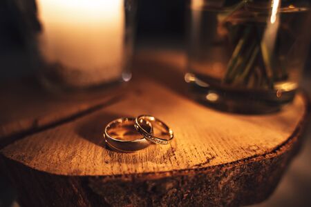 Pair of decorated wedding rings laying on wood. Warm tones by candle light. Shallow depth of field. Orange toned.の写真素材