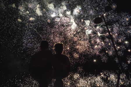 Rear view of pair watching amazing huge fireworks. Man and woman embracing and enjoying celebration.の写真素材