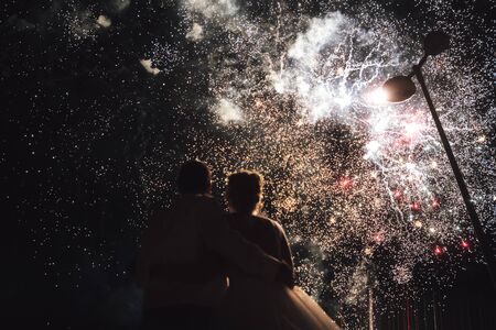 Rear view of couple watching amazing huge fireworks. Newlyweds embracing and enjoying their wedding celebration.の写真素材