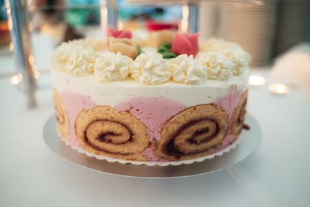 White wedding cake standing on festive table. Closeup of roulade tier decorated with white and pink...