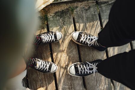 Two pairs of legs wearing black and white sneakers standing on wooden boardwalk. Wedding couple in...