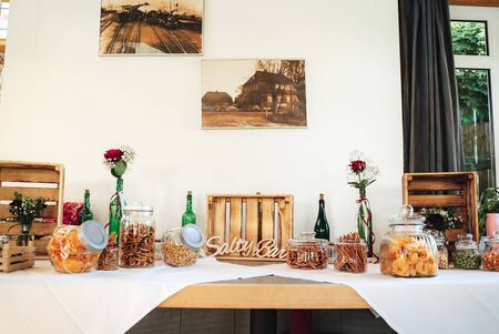 Salty bar of several kinds of nuts, potato chips, salted pretzels, sticks and snacks decorated on wooden table inside room. Wedding or party concept.の写真素材
