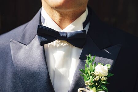 Close up shot of man in white shirt and blue suit with blue bow tie and flower wedding boutonniere....