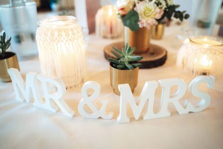 Festive wedding table decoration. Flowers, candles in glass lamps and standing lettering Mr. and Mrs. on white table cloth. Celebration and weddingの写真素材
