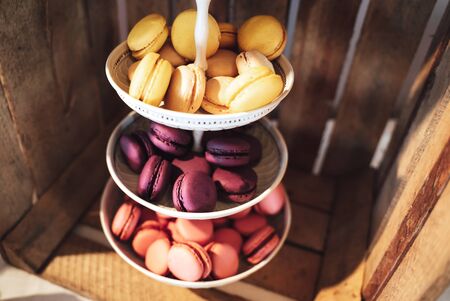 Three tiered plate stand with colorful sweet macaroons. Wooden plant box background. Dessert for served with afternoon tea or coffee. Wedding or partyの写真素材