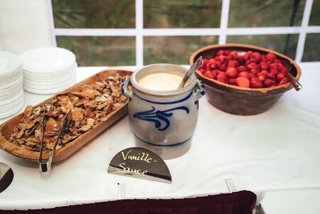 Sweet snack. Jug of vanilla sauce and bowl of fresh strawberries on self-serving buffet table. Celebration, party, birthday or wedding concept.の写真素材