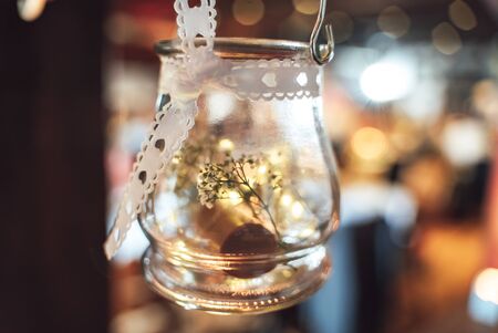 Hanging round glass container used as vase decorated with white ribbon with hearts. Abstract blurred...