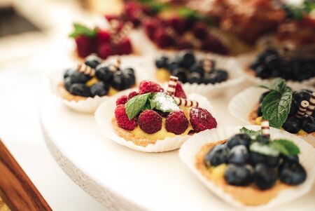 Delicious miniature cakes in buffet trays. Raspberry, blueberry decorated cupcakes. Various desserts at party. Celebration, party, birthday or weddingの写真素材