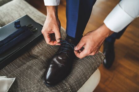 Close up of groom tying laces on brown leather shoes. Businessman in formal wear tie up shoelace on elegant shoes. Low section view.の写真素材
