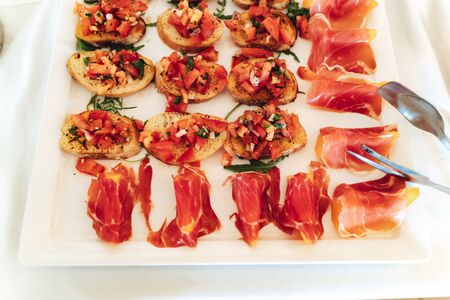 Top view of white tray with delicious mini sandwich snacks and fruit rolled in ham. Self-service buffet table. Celebration, party, birthday or weddingの写真素材