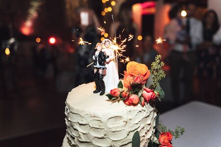 Close up of figurines: tied up and locked groom and bride with key. Marriage cake decorated with colorful fresh roses, wedding pair topper.の写真素材