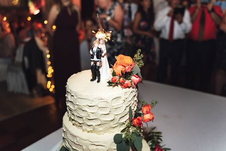 Wedding cake close up. Sweet cake decorated with colorful fresh roses and marriage couple topper. Figurines of tied up groom and bride with key.の写真素材