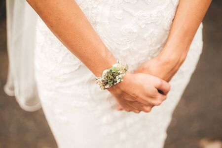 Close up of caucasian brides hands with floral bracelet over white lace wedding gown. Wedding day concept.の写真素材