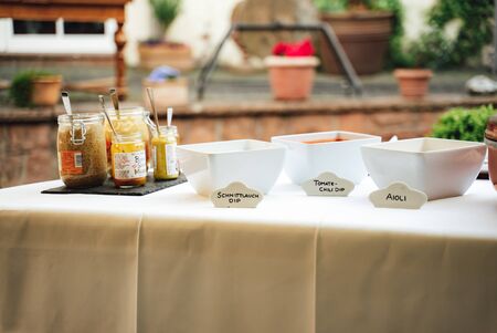 Table with various sauces and dips in glasses and white square bowls. Translation: Schnittlauch...