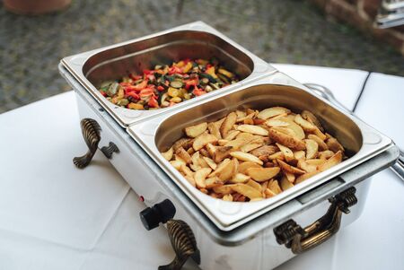 Fried american potatoes and mix of grilled vegetable in hotel pans on food warmer. Self-service buffet table. Celebration, party, birthday or weddingの写真素材